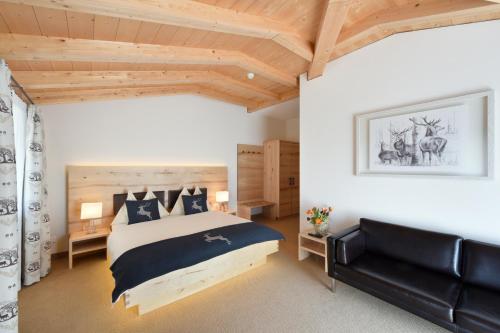 a bedroom with a large bed and a black leather couch at Hotel Cervo in Sils Maria