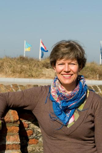 a woman wearing a scarf is standing on a brick wall at Hotel Steeds aan Zee in Katwijk