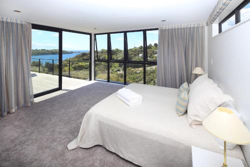 a bedroom with a large bed and large windows at Blackwood Retreat in Oneroa