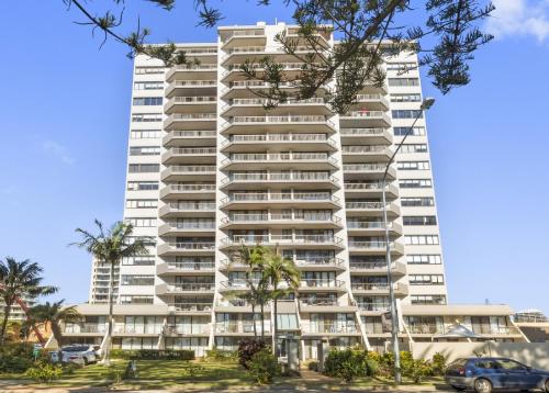 a tall white building with palm trees in front of it at Columbia Beachfront Apartments on Rainbow Bay in Gold Coast