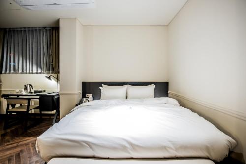 a bedroom with a large white bed and a desk at Rivertain Hotel in Daegu
