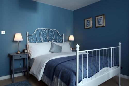 Dormitorio azul con cama blanca y pared azul en Coach Road Cottages en Comber