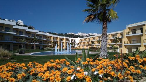 a large building with a palm tree and flowers at Apartamento O Jardins da Marina in Albufeira