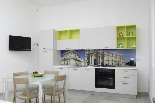 Una cocina con gabinetes blancos y una mesa con sillas. en Casa Vacanze Ortigia, en Siracusa