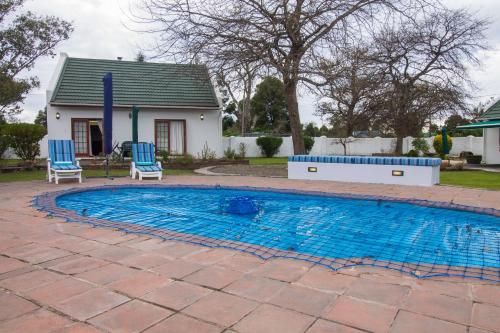 a swimming pool with two blue chairs and a house at Swallows Nest Country Cottages in Stormsrivier