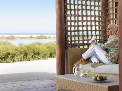a woman sitting on a porch with a table at Anantara Sir Bani Yas Island Al Yamm Villa Resort in Da‘sah