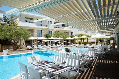 uma piscina com mesas e cadeiras brancas ao lado de uma piscina em Renaissance Hanioti Resort em Hanioti