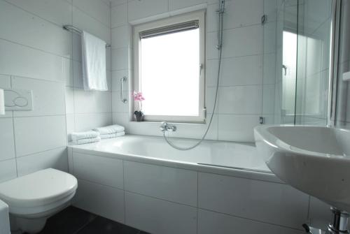 a white bathroom with a tub and a toilet and a sink at Hotel Restaurant de Sleutel in Riethoven