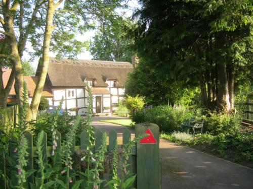 a house with a fence with a red triangle on it at THE MOATS - CODDINGTON A small private thatched cottage B&B located in quiet countryside between Ledbury and Malvern - convenient for the Malvern Three Counties Showground and 5 miles from excellent shops restaurants and Ledbury Poetry Festival in Ledbury