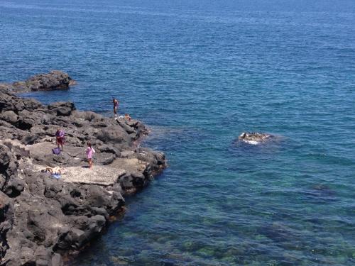 a group of people standing on rocks in the water at Il Giardino Dei Limoni in Aci Castello