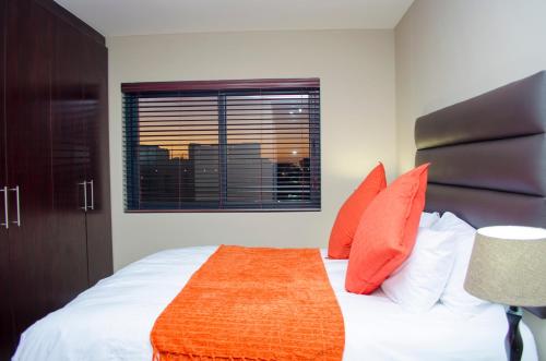 a bedroom with a bed with orange pillows and a window at Knightsbridge Luxury Apartments in Cape Town