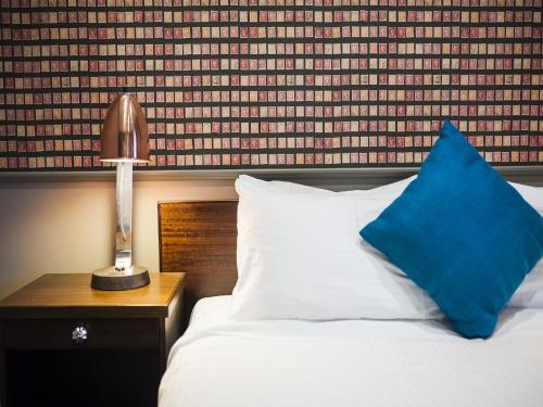 a bed with a blue pillow and a lamp on a table at Criterion Hotel Sale in Sale