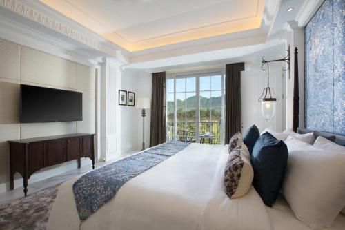a bedroom with a large white bed with a flat screen tv at Plataran Heritage Borobudur Hotel in Borobudur