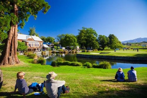 a group of people sitting in the grass by a river at Millbrook Resort in Arrowtown