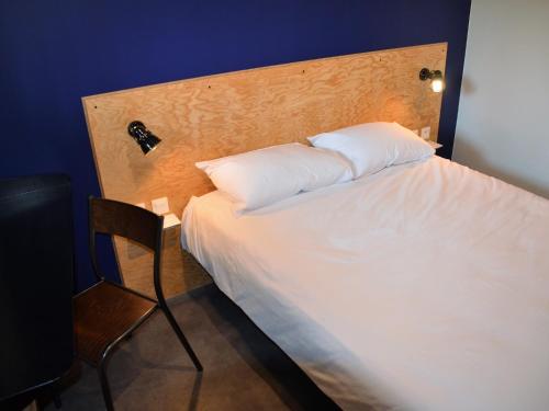 a white bed with a wooden headboard and a chair at Eklo Hotels Lille in Lille