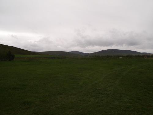 a large green field with mountains in the background at Miðhvammur Farm Stay in Aðaldalur