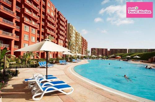 a large swimming pool with chairs and an umbrella at Apartment in Golf Porto Marina in El Alamein