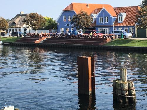 a group of people sitting on benches next to a body of water at Enø Bageri's Hotelværelser in Karrebæksminde
