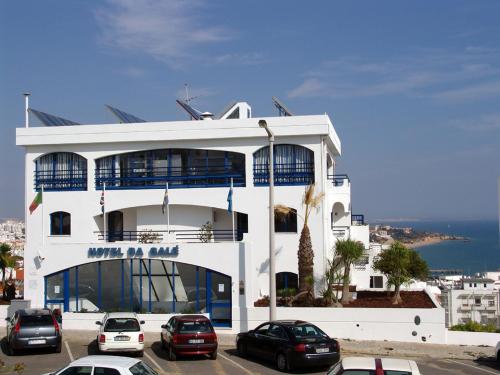 a white building with cars parked in a parking lot at Hotel da Gale in Albufeira