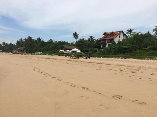 a beach with tables and umbrellas and a house at Talalla Bay Beach in Talalla