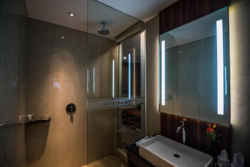 a bathroom with a shower and a sink and a mirror at Arthama Hotels Makassar in Makassar