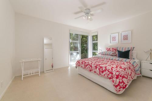a white bedroom with a bed and a ceiling fan at Ted's Cottage near Little Oneroa Beach by Waiheke Unlimited in Oneroa