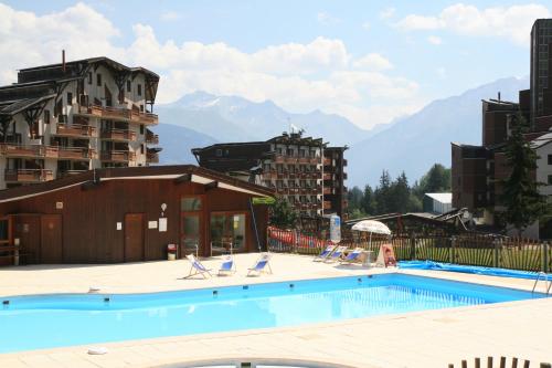 une piscine avec des chaises et des montagnes en arrière-plan dans l'établissement Résidence Grand Bois Clés Blanches, à La Tania