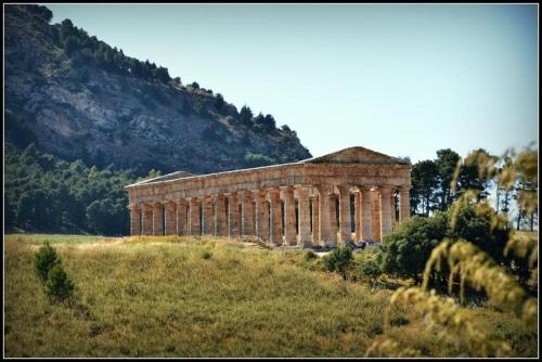 a building on a hill in a field with a mountain at Grace's Place in Scopello