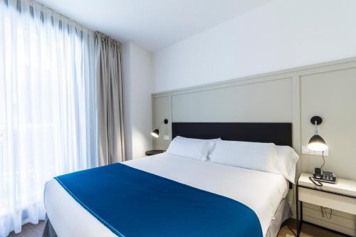a bedroom with a blue and white bed and a window at Hotel SANSEbay in Donostia-San Sebastián