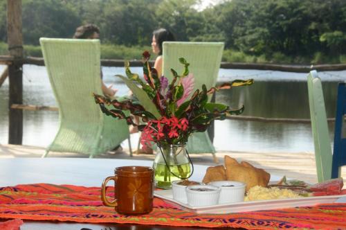 a table with a vase of flowers and a plate of food at Lamanai Hotel & Marina in Orange Walk