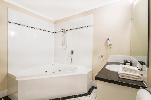 a white bathroom with a tub and a sink at Regal Port Douglas in Port Douglas
