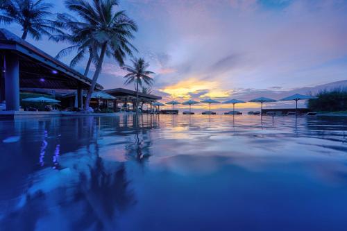 a sunset over a pool with palm trees and umbrellas at Anantara Mui Ne Resort in Mui Ne