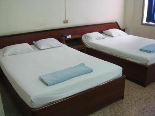 2 camas con sábanas blancas y una almohada azul. en Ho Fah Hotel, en Phatthalung