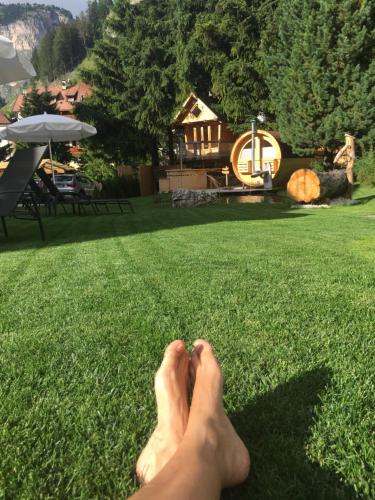 a persons feet on the grass with a house in the background at Chalet Elisabeth dolomites alpin & charme in Selva di Val Gardena