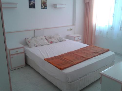 a bedroom with a white bed with an orange blanket on it at Aygun Apartment 2 in Mahmutlar