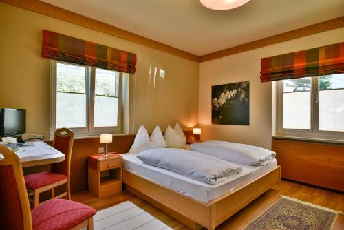 a bedroom with a bed and a desk and two windows at Hotel Villnerhof in Egna