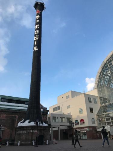 a pole in the middle of a street with people walking around at Guest House On My Way in Sapporo