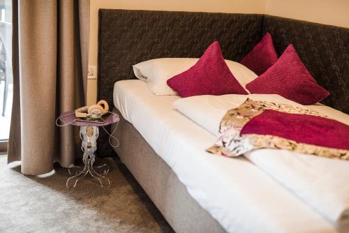 a bed with red and white pillows and a side table at Hotel Restaurant Kirchsteiger in Vollan
