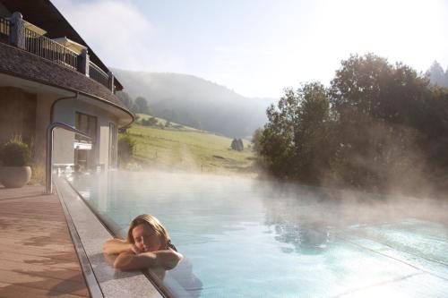 a woman laying in a hot tub next to a building at Hotel Heselbacher Hof in Baiersbronn