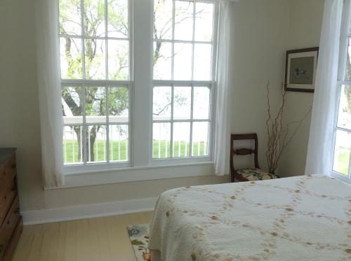 a bedroom with a bed and two large windows at Wades Point Inn on the Bay in Saint Michaels