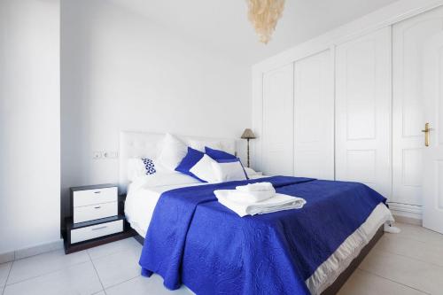 a white bedroom with a blue bed with a blue blanket at Bright villa with salt water pool in El Campello