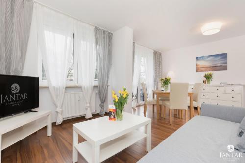 a living room with white furniture and a tv at Jantar Apartamenty City Center 2 in Kołobrzeg