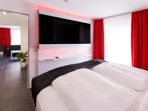 um quarto com uma cama branca e uma televisão de ecrã plano em DORMERO Hotel Villingen-Schwenningen em Villingen-Schwenningen