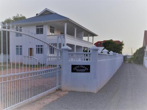 a white fence in front of a white house at Didi's Dream apartments in Anse Kerlan
