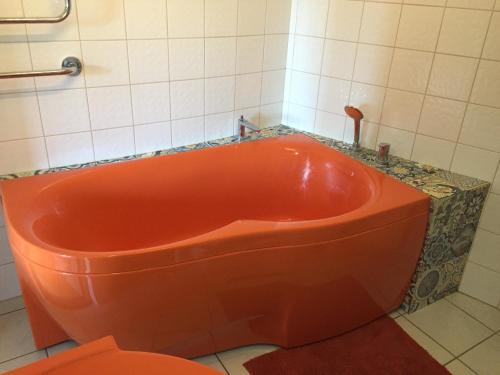 an orange tub in a bathroom with a tiled wall at Peahen Residence in Sigulda