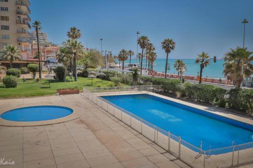 a swimming pool with palm trees and the ocean at Piso Paseo Marítimo in Benalmádena