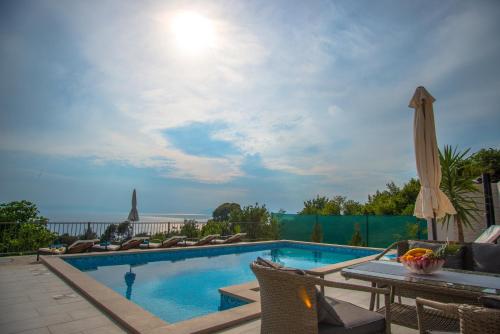 a swimming pool with chairs and an umbrella at Vila Divna in Podgora