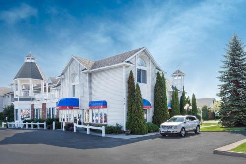 a white house with a car parked in a parking lot at Ramada by Wyndham Mackinaw City Waterfront in Mackinaw City