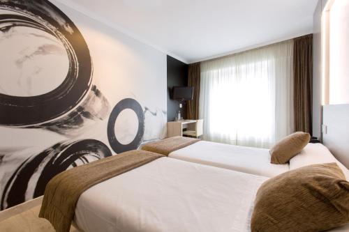 two beds in a hotel room with a picture on the wall at Hotel Alda San Carlos in Santiago de Compostela