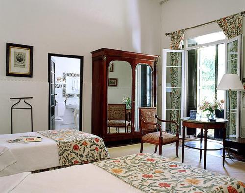 a bedroom with two beds and a mirror and a chair at Palacio de la Rambla in Úbeda